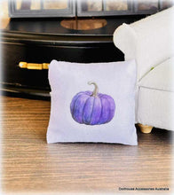 Decorative dollhouse miniature pillow with a purple pumpkin design on a wooden floor.