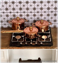 Set of copper pots and pans on a stove against a tiled wall.