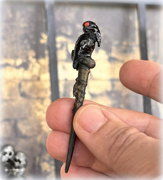 A 1:12 scale dollhouse miniature accessory featuring a red-eyed crow's head on a wand or walking cane, held in a person's hand.