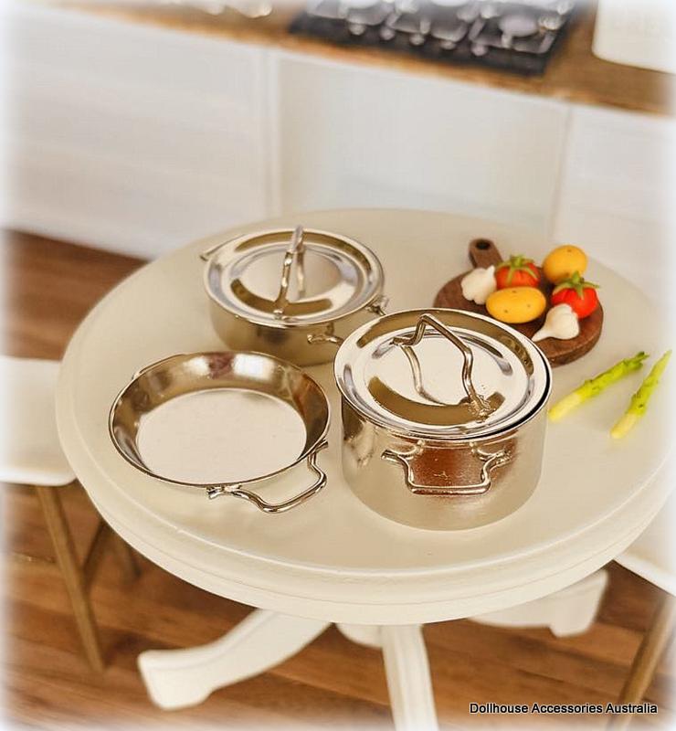 Set of silver pots and pans on a small round table with miniature food items.