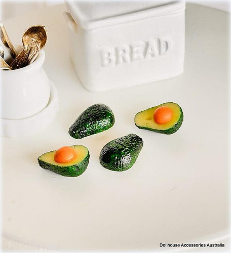 Miniature avocado slices with an orange center on a white surface, resembling food for a dollhouse.