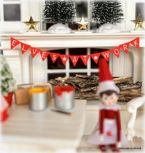 Elf on the shelf with 'ELVES AT WORK' banner in a festive room.