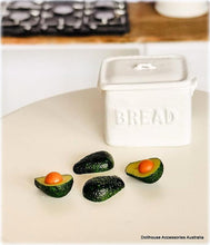 Avocados with orange slices on a white surface next to a white bread container.