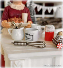 Miniature kitchen Christmas baking scene with a doll, cups, and utensils on a table.