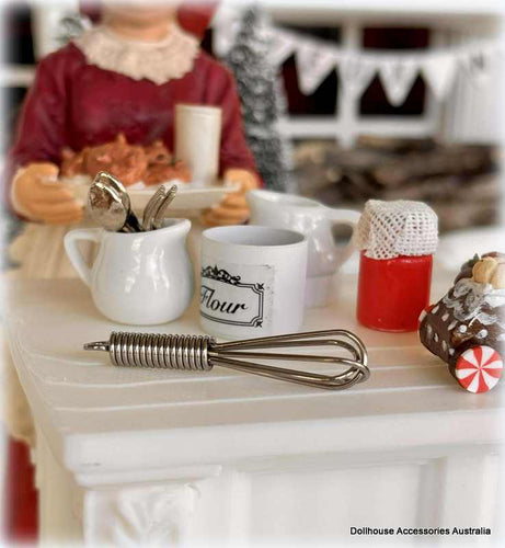 Miniature kitchen Christmas baking scene with a doll, cups, and utensils on a table.