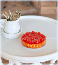 Miniature cherry tart on a white surface with a cup of gold forks in the background.