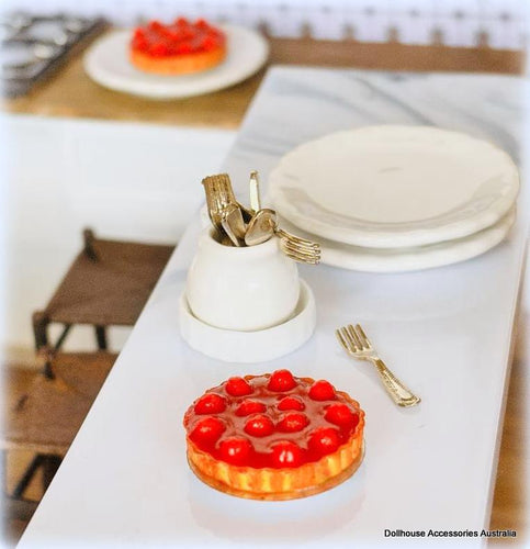Miniature table setting with a cake, plates, and cutlery on a white surface.