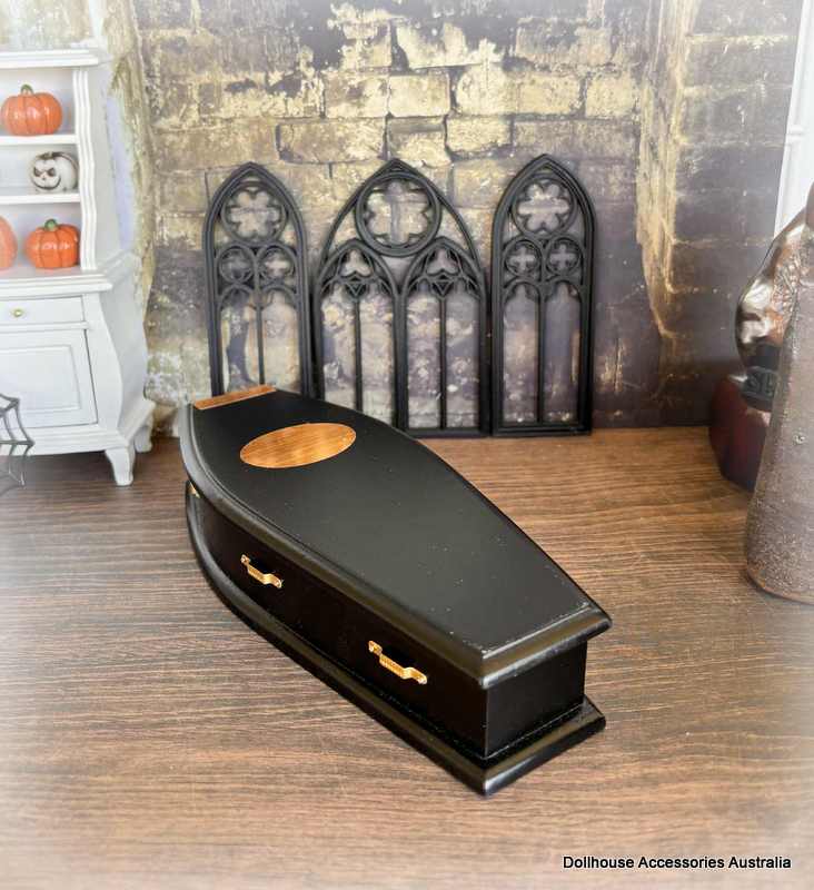 Black coffin with gold accents on a wooden floor, Gothic-style fireplace in the background.