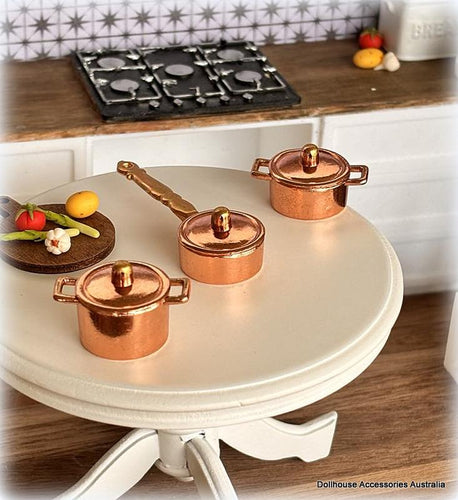 Set of miniature copper pots on a round table with a kitchen background.