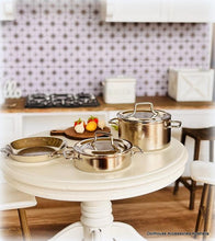 Set of stainless steel pots and pans on a kitchen counter with a checkered backsplash.