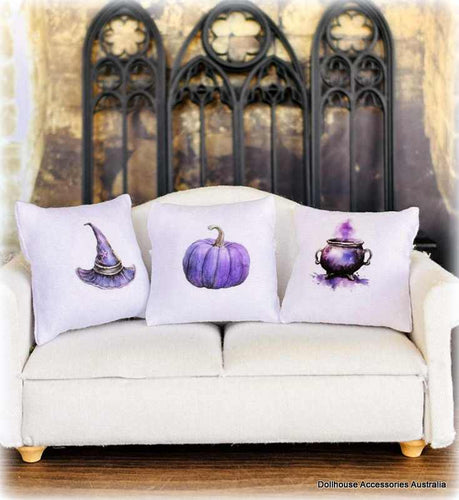 Three Halloween-themed pillows on a white couch with a witches dollhouse cottage
